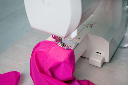 Close up of sewing machine working with pink fabric and pins on a table. Home hobby and business. Repair of clothes.の写真素材