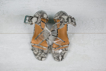 Women snake leather skin shoes with high heels on light wood background. Black and white sandals...