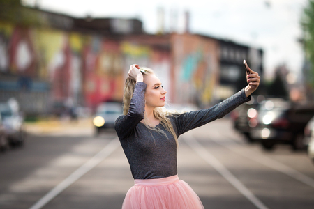 Young smiling cheerful blonde girl making selfie while standing on the streetの写真素材