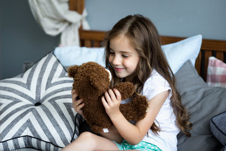Cute little girl is playing with a toy bear on the bedの写真素材