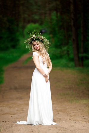 Portrait of a beautiful bride in a white dress and a wreath of Forest flowersの写真素材