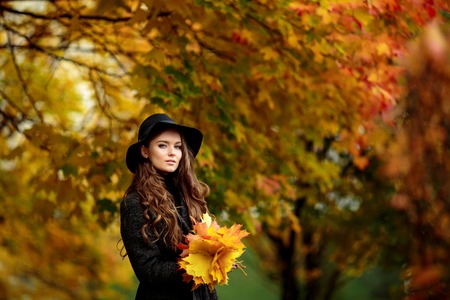Woman with autumn leaves in hand and fall yellow maple garden background. Portrait of very beautiful young girl in autumn park.の写真素材
