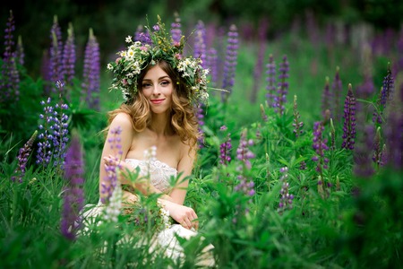 Beautiful young woman in white dress in lupine fieldの写真素材