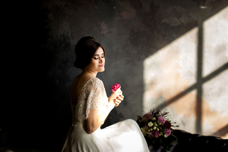 Bride in beautiful dress sitting on chair indoors in dark studio interior like at home.の写真素材