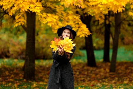 Young woman with autumn leaves in hand and fall yellow maple garden backgroundの写真素材