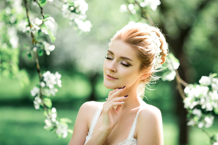 Beautiful girl hands with a branch of a blossoming apple tree. Young beautiful blonde woman in blooming garden. Bride.の写真素材