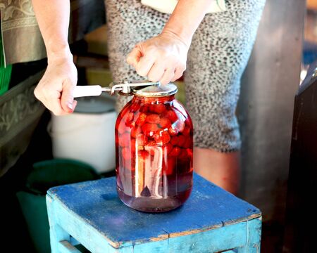 female hands put compote in a glass three-liter jar with a compote of summer aroma of bright red strawberries in an old wooden house, making harvests for the winterの写真素材