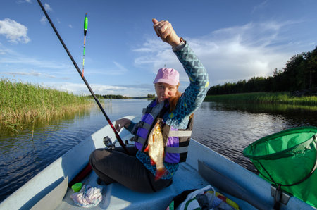A woman sitting in the fisherman boat. She caught a fish on a bait.