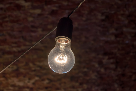 Light bulb hanging on a electric cable in front of a brick wallの写真素材
