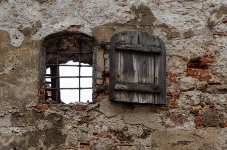 An old wall with sprinkled plaster. The window in the wall has an old wooden door. Riga. Latvia.の写真素材