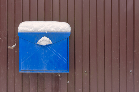 A blue metal mailbox on a brown fence. On the mailbox is a layer of snow. Background. Structure.の写真素材