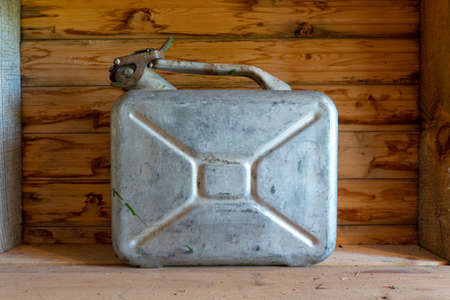An old metal canister for flammable liquids is on the floor. In the background there is a wall of aged, unpainted boards. Background. Texture.の写真素材