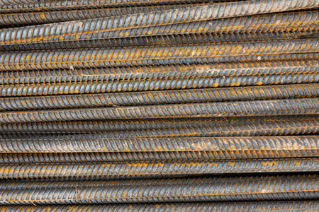 Many steel bars are laid horizontally. Rust is visible on the ribbed metal surface. Background....