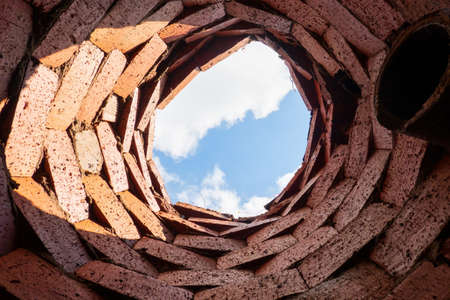 A look up from a primitive drainage well. The walls are made of rough plain bricks and there is a drain pipe. A fragment of the sky is visible at the top. Background. Texture.の写真素材