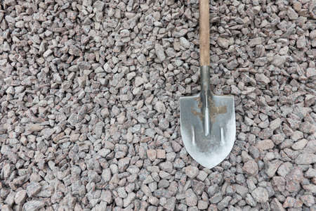 A shovel with a wooden handle rests on a pile of gray and pink granite stones for construction. Background. Texture.の写真素材