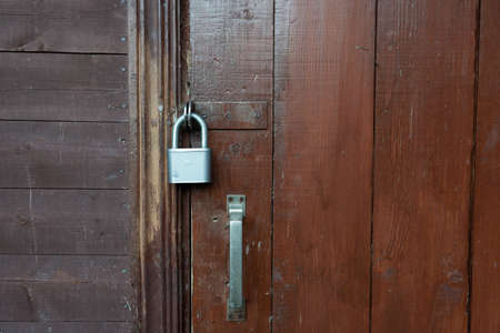 The brown wooden door of the village house is padlocked. Part of the wall is visible, sheathed with horizontal boards. Background. Texture.の写真素材
