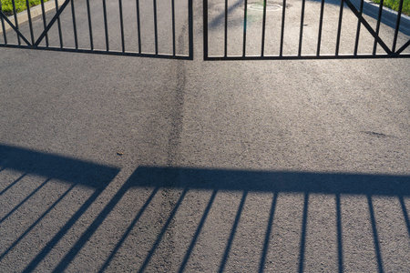 Welded metal gates block the asphalt road. Only the lower part is visible. There is a shadow from...