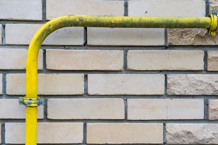 The yellow gas pipe is bent at right angles and is attached to a brick wall. The paint is covered with dirt in places. There are individual rustic bricks. Background. Texture.の写真素材