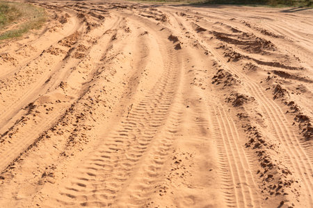 A fragment of a rural road made of loose pink sand. There are deep grooves and tread marks from passing vehicles. Background. Texture.の写真素材