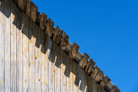 The edge of the roof of an old wooden house against a blue cloudless sky. On the wall are visible...