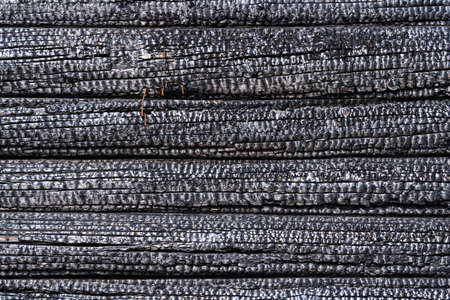 Burnt wall of a wooden house made of logs. The surface is covered with a black charred layer. Background. Texture.の写真素材