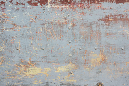 Fragment of a metal surface with rivets. Several layers of old paint of different colors are...