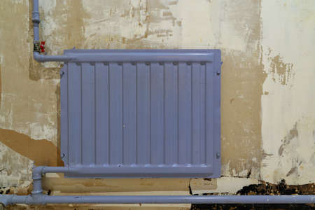Old blue radiator and pipes of the heating system in the room during renovation. A plasterboard wall in the background with the wallpaper removed. Background.の写真素材