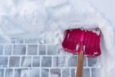The view from the eyes of a person cleaning a thick layer of snow on a paving slab. There is a red plastic shovel with a wooden handle. Background.の写真素材
