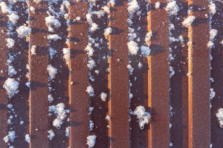 The brown metal fence is illuminated by the winter sun. There is frost and adhered snow flakes on the surface. Background. Texture.の写真素材