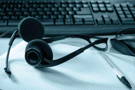 Close-up of a workplace with a computer. There is a keyboard, notepad, headset and mouse. Illuminated with blue light. background. concept. business.の写真素材