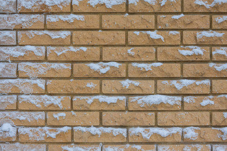 Fragment of a wall made of yellow decorative brick. Flakes of fresh snow stuck to the vertical...