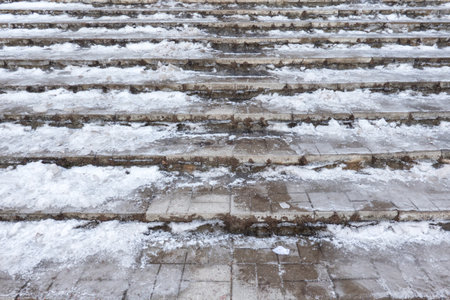 Close-up of the stairs going up. The gray tile steps are covered with a layer of ice and snow. There is a well-trodden path in the middle. Background.の写真素材