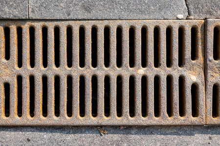 Fragment of a cast iron grating of a drainage ditch in a granite pavement. Close-up. Background.