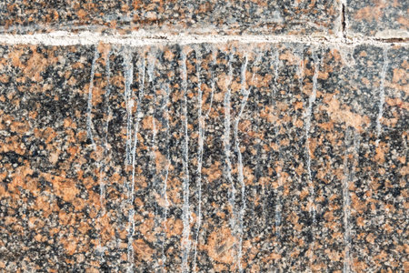 A fragment of a red and black granite wall with white streaks of anti-icing mixture. City....