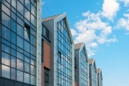 Fragment of the facade of a modern building. The glass windows reflect the blue sky with clouds....