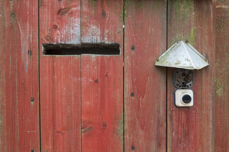 Fragment of a red old wooden wall with a post hole and an electric bell. Background. Close-up. Grungeの写真素材