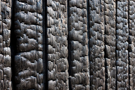 A perspective view of a burnt wall of a wooden house. Black boards covered with charcoal....