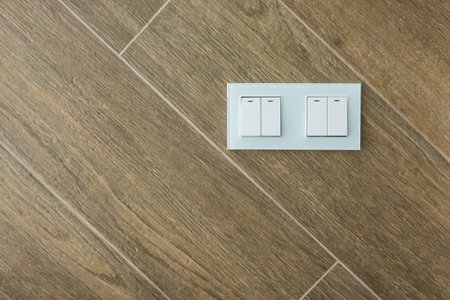 White electric switch with four keys on the wall finished with brown large ceramic tiles. The...