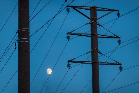 Poles and wires of the power line against the blue evening sky. There is a moon. Background.の写真素材
