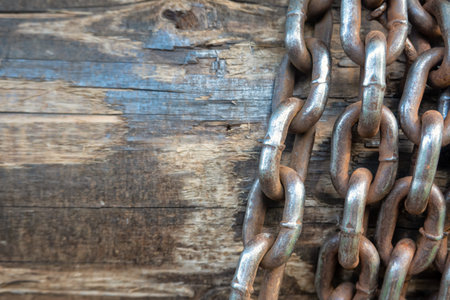 Close-up of an old steel chain wound around a wooden well shaft. The links are worn and...