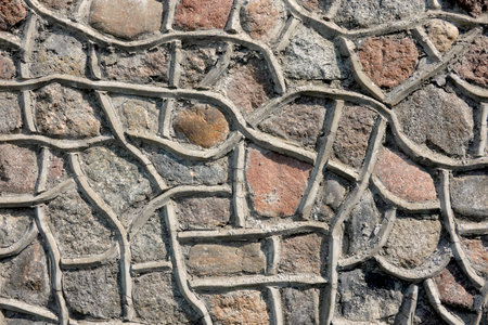 Fragment of a wall of an old building made of natural stones. There is a decorative finish of cement...
