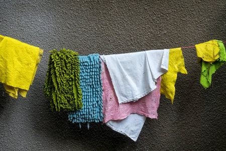 Multicolored cleaning rags are drying on a rope against a gray wall. Background. Texture.