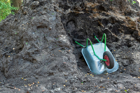 An overturned metal wheelbarrow lies in a pile of dark agricultural soil. Background.の写真素材