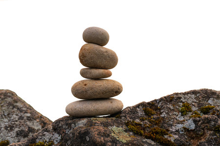Pyramid of gray flat stones stands on rough stone surface covered with moss and lichen. Isolated on white. Background.の写真素材
