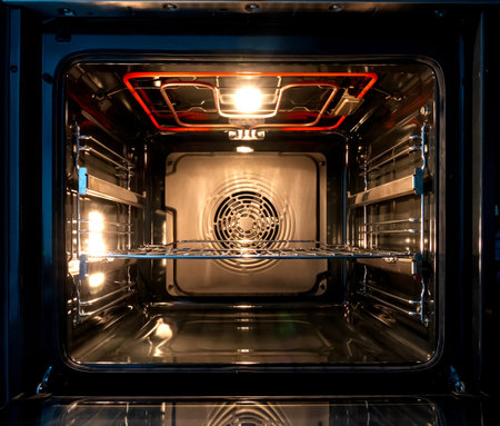 A look inside an open kitchen electric oven. There is a red hot heater, a light is shining....