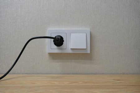 A white electrical outlet with a switch on the wall. A black cord with an electrical plug is...
