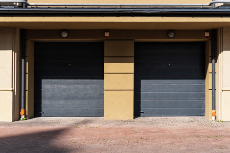 Two garages in a modern stone house are closed with gray roller shutters. Geometric shadows are...