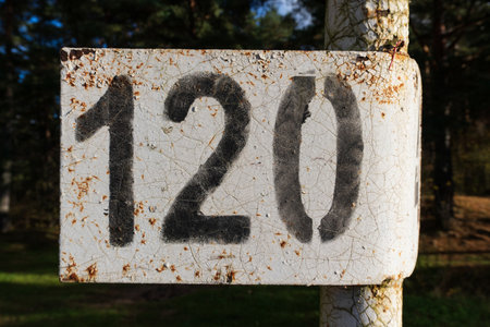 An old kilometer sign by the road with the inscription 120. The white surface of the sign is cracked, rust is visible. Background.の写真素材