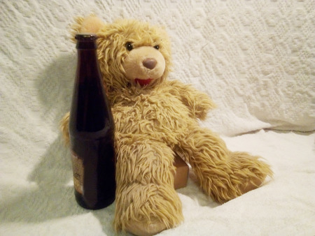 happy toy bear on white background sitting with a bottle of beerの写真素材
