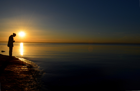 silhouette of a man who prays against the backdrop of a beautiful setting sun by the seaの写真素材